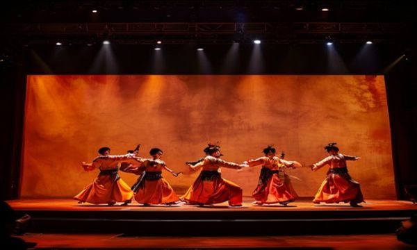 传统戏曲舞台上演员在橙黄灯光下展示打女生屁股程式化动作，古典服饰与精准身段呈现戏剧张力